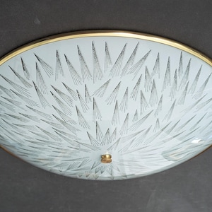 May include: A round, flush-mount ceiling light fitting featuring a frosted white glass dome with a black, radiating starburst or needle-like pattern. The glass is secured by a thin, polished brass rim and a small, centred brass finial knob.
