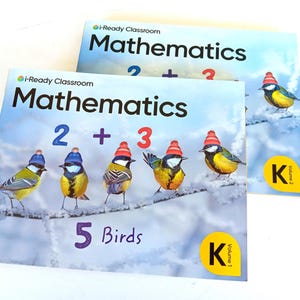 May include: Two i-Ready Classroom Mathematics textbooks for kindergarten. The front covers feature five birds wearing red knit hats perched on a snowy branch, the text 2 + 3, and the text 5 Birds. One book is labeled Volume 1 and the other Volume 2.