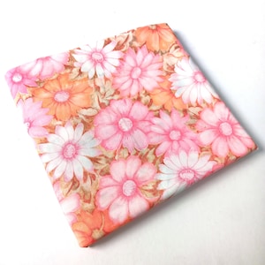 Puede incluir: Tela doblada con un estampado floral de grandes margaritas en tonos rosa, naranja y blanco. Las flores se destacan sobre un fondo de follaje marrón y verde.