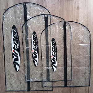 May include: Four clear garment bags with black zippers and the "Nitro Racing" logo in white and red. The bags are made of a transparent material, allowing visibility of the contents. The bags are different sizes.