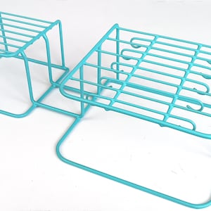 May include: A two-tiered turquoise metal shelf unit with a square base and a rectangular top shelf. The shelf unit is made of wire and has a simple design.
