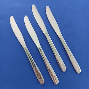 Puede incluir: Cuatro cuchillos de mantequilla plateados con diseños florales sobre un fondo azul.