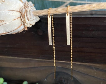 May include: A pair of gold dangle earrings with thin, rectangular bar pendants hanging from delicate chains.