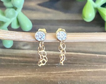 May include: A pair of gold earrings with a small round clear stone and a dangling chain.
