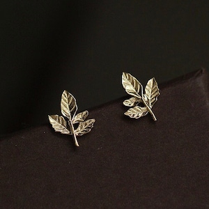 May include: A pair of gold leaf earrings. Each earring features three delicate leaves connected by a thin stem.