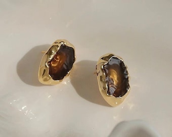 May include: A pair of gold-toned earrings with brown, irregular-shaped glass stones. The earrings have a textured, organic look.