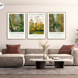 May include: Three framed art prints of landscape paintings by Camille Pissarro. The prints feature a river scene with trees and a bridge in the background. The prints are in a modern living room setting with a couch and coffee table.