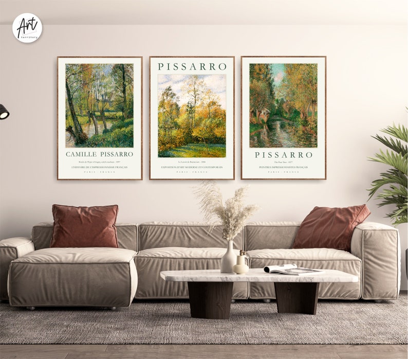 May include: Three framed art prints of landscape paintings by Camille Pissarro. The prints feature a river scene with trees and a bridge in the background. The prints are in a modern living room setting with a couch and coffee table.
