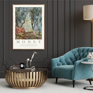 Op de afbeelding: Een ingelijste poster van een schilderij van Claude Monet met de titel "De olijfgaarden in het domein van Saint-Clair, 1884." De poster toont een landschapssc&egrave;ne met olijfbomen en een pad dat de diepte in loopt. De tekst "MONET" is in grote letters onderaan de poster gedrukt.