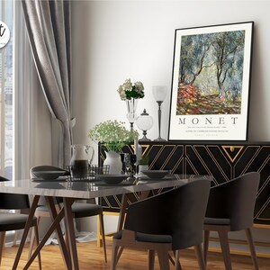 Op de afbeelding: Een zwart en gouden dressoir met een geometrisch patroon en een ingelijste print van een schilderij van Claude Monet met de titel "De olijfgaard in het domein van Saint-Clair, 1884". De print toont een landschapssc&egrave;ne met olijfbomen en een pad.