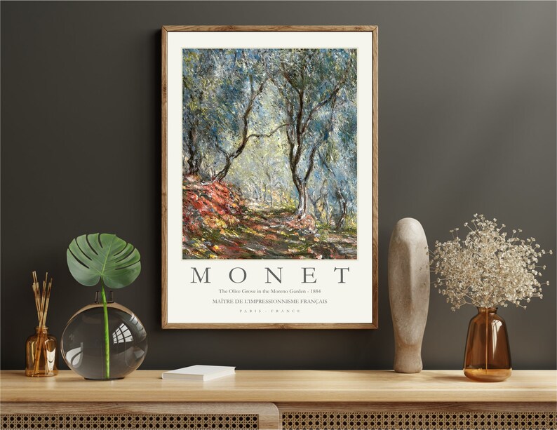 Op de afbeelding: Een ingelijste print van een schilderij van Claude Monet met de titel "The Olive Grove in the Montross Garden - 1884". Het schilderij toont een olijfgaard met een pad dat er doorheen loopt. De bomen zijn geschilderd in tinten groen en blauw, met hints van geel en oranje. De tekst "MONET" is in grote letters onder het schilderij gedrukt, samen met de titel en de informatie over de kunstenaar.