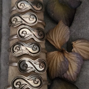 May include: Six silver rings with an infinity symbol design. Each ring features a swirling pattern within the infinity symbol.