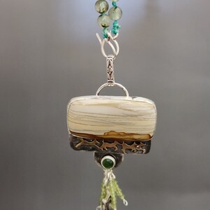 May include: A silver pendant necklace with a rectangular white and brown agate stone, a green stone, and a silver tassel. The necklace is made of green and white beads.