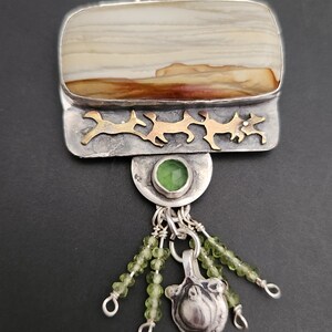 May include: A silver and gold pendant necklace with a brown and white agate stone, green gemstone accents, and a silver charm. The pendant is attached to a silver chain.