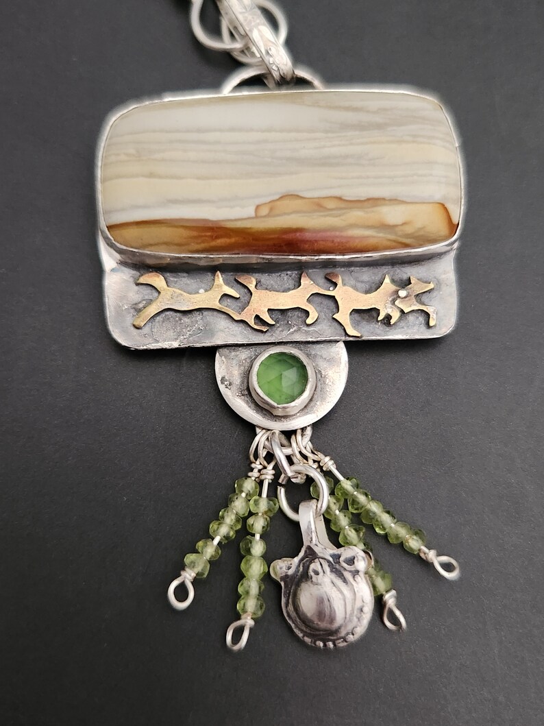 May include: A silver and gold pendant necklace with a brown and white agate stone, green gemstone accents, and a silver charm. The pendant is attached to a silver chain.