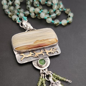 May include: A silver pendant necklace with a rectangular agate stone, green gemstone accents, and a silver charm with a beaded tassel. The necklace is made with green and black beads.