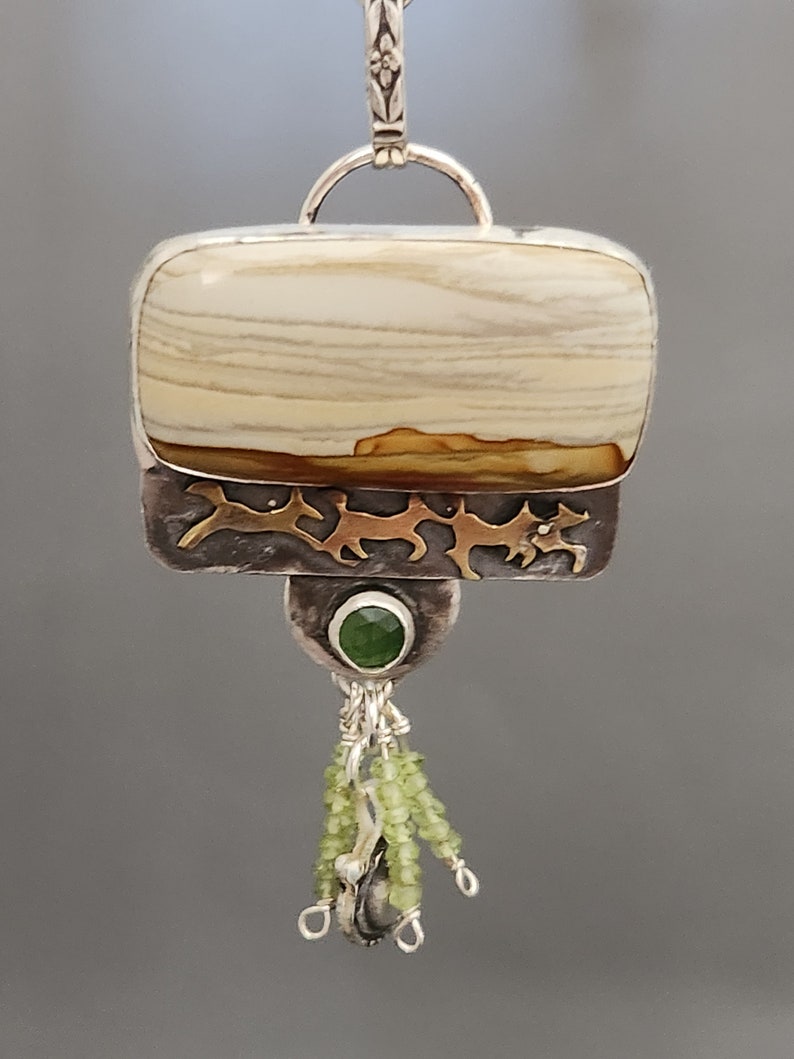 May include: A silver and gold pendant with a beige and brown agate stone, a green gemstone, and green beads hanging from the bottom.