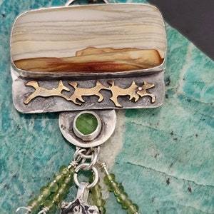 May include: A silver and gold pendant necklace with a rectangular agate stone, a green gemstone, and a silver charm. The pendant is hanging from a silver chain.