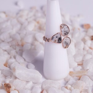 May include: A rose gold ring featuring a cluster of three large, irregular, grey diamonds and smaller round diamonds set in the band.