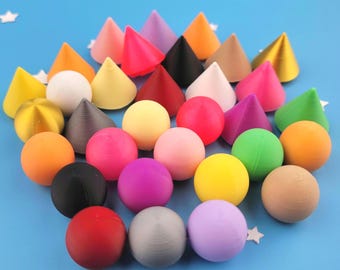 May include: A collection of small, solid objects in two distinct shapes: smooth spheres and pointed cones. These items come in a wide variety of vibrant colors, including red, orange, yellow, green, blue, purple, pink, black, white, and tan.