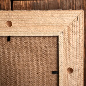 May include: Close-up of a wooden frame with a brown canvas backing. The frame has two visible holes on the top and right side.