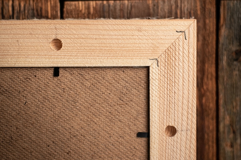 May include: Close-up of a wooden frame with a brown canvas backing. The frame has two visible holes on the top and right side.