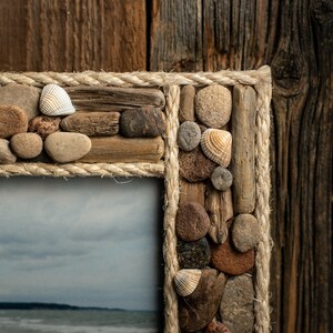 May include: A rustic picture frame made from driftwood, stones, and rope. The frame is decorated with seashells and has a natural, beachy aesthetic.