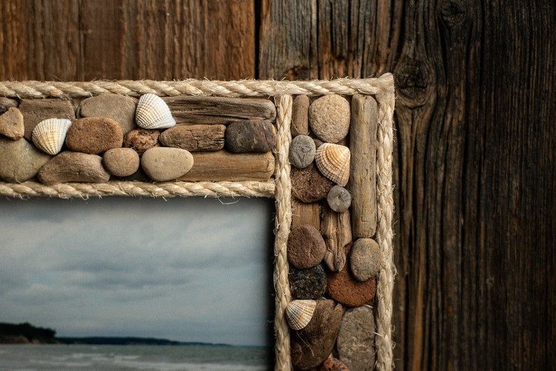 May include: A rustic picture frame made from driftwood, stones, and rope. The frame is decorated with seashells and has a natural, beachy aesthetic.