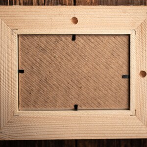 May include: A natural wood picture frame with a light brown finish. The frame has a simple design with a smooth surface and a rectangular shape. The frame is empty and ready to display a photo or artwork.