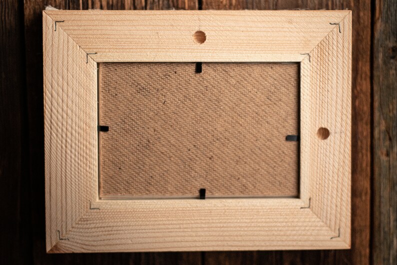 May include: A natural wood picture frame with a light brown finish. The frame has a simple design with a smooth surface and a rectangular shape. The frame is empty and ready to display a photo or artwork.