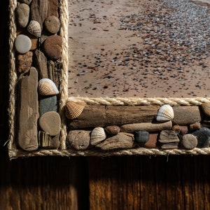 May include: A wooden picture frame decorated with driftwood, rope, and seashells. The frame is a light brown color and the seashells are white and beige.
