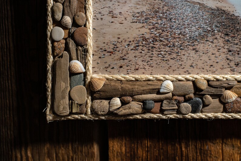 May include: A wooden picture frame decorated with driftwood, rope, and seashells. The frame is a light brown color and the seashells are white and beige.