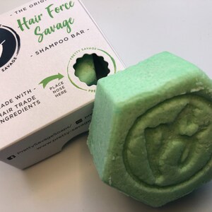 May include: A green shampoo bar with the words "Hair Force Savage" and "Shampoo Bar" printed on the packaging. The bar is in a hexagonal shape with a circular design in the centre.