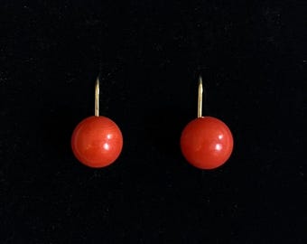 May include: A pair of drop earrings featuring smooth, spherical red beads suspended from thin, gold-toned metal hooks. The earrings are symmetrical, each consisting of a single round red bead attached to a curved wire finding for attachment.