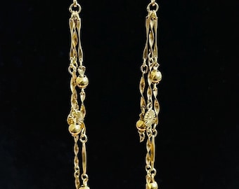 May include: Gold-toned dangle earrings with intricate detailing. Each earring features a series of delicate chains, small beads, and decorative elements. The earrings are suspended from a lever-back closure, creating a flowing, elegant design.