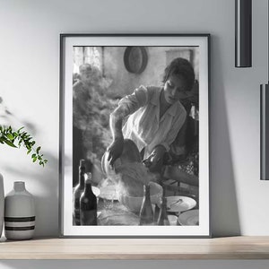 Può includere: Fotografia in bianco e nero di una donna che versa liquido da una brocca in una ciotola. La donna indossa una camicia bianca e si trova in una cucina.