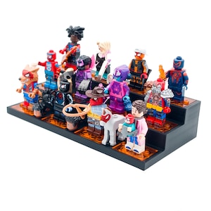 Può includere: Una collezione di colorate minifigure Lego, tra cui supereroi e altri personaggi, è esposta su una piattaforma nera a più livelli. Le figure presentano una varietà di costumi e accessori, creando una scena vibrante e dettagliata.