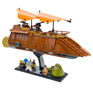 Peut inclure: Un ensemble Lego Star Wars comprenant un grand Sand Crawler brun et orange avec un support noir. L'ensemble comprend plusieurs figurines, dont Jabba le Hutt, un Tusken Raider et un Jawa.