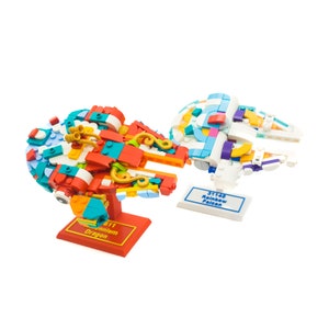 Puede incluir: Dos modelos de Lego Millennium Falcon de colores, uno rojo y otro blanco, con los nombres "Millennium Dragon" y "Rainbow Falcon" en sus bases.