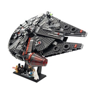 Op de afbeelding: Een zwart en rood LEGO Millennium Falcon ruimteschip met een standaard en minifiguren. Het schip heeft een gedetailleerd ontwerp met een rode motor en een zwart en grijs exterieur.