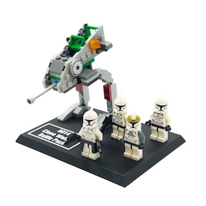 Può includere: Un set Lego Star Wars Clone Wars Battle Pack con un walker AT-RT grigio e verde con un cannone blaster blu e quattro minifigure di clone trooper bianche. Il set include una base di esposizione nera con il testo "8014 Clone Wars Battle Pack".