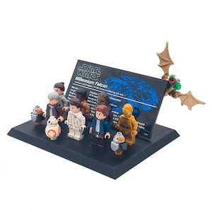 Puede incluir: Un set de Lego Star Wars Millennium Falcon con múltiples minifiguras y una tarjeta de exhibición. El set incluye personajes como Han Solo, Chewbacca y C-3PO. Las figuras están dispuestas sobre una base negra con una criatura alada marrón y beige.
