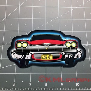 Puede incluir: Una pegatina de coche roja y negra con un brillo azul alrededor. El coche tiene una matrícula que dice "COB 241".