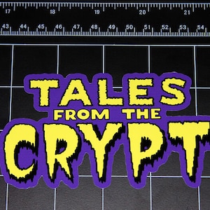 Può includere: Un adesivo viola e giallo con il testo "TALES FROM THE CRYPT" in un font a goccia.