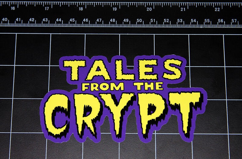 May include: A purple and yellow sticker with the text "TALES FROM THE CRYPT" in a dripping font.