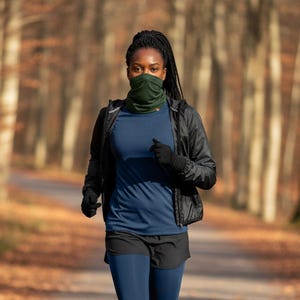 Może przedstawiać: Osoba biegnąca ścieżką przez las, ubrana w odzież sportową. Strój obejmuje granatową koszulkę, czarne szorty i granatowe legginsy. Akcesoria obejmują czarną kurtkę, rękawiczki, zielony ocieplacz na szyję i niebieskie buty do biegania.