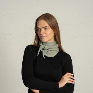 Könnte beinhalten: Eine Frau trägt ein schwarzes Langarmshirt und einen hellgrünen Halstuch. Der Schal ist vorne geknotet. Die Frau hat lange, hellbraune Haare und schaut zur Seite.