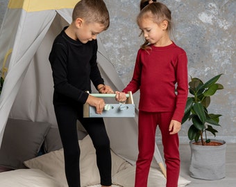 Puede incluir: Un conjunto de camisetas de manga larga y leggings térmicos a juego en colores negro sólido y rojo intenso. Las prendas presentan una textura acanalada, cuellos redondos y puños ajustados para brindar calidez y comodidad.