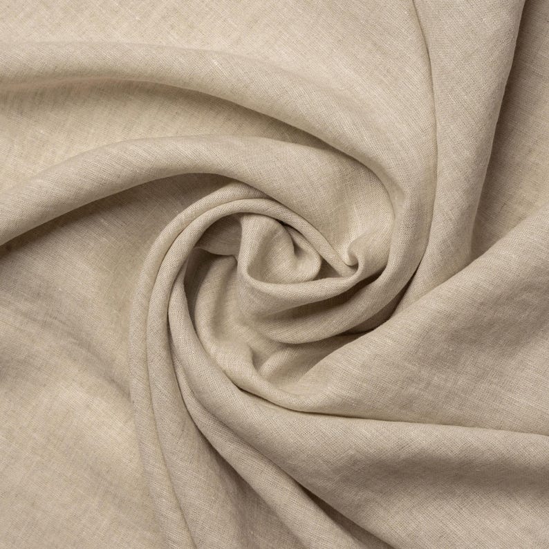 Pu&ograve; includere: Un primo piano di un tessuto di lino beige, che mostra la sua texture naturale e il suo morbido drappeggio.