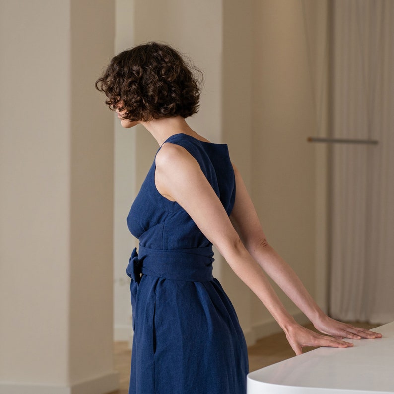 Photograph features a woman wearing the HAILEY summer wrap dress in storm blue color. The model is seen from the side, featuring the sleeveless design ant the waistline of the dress. The side pocket is visible as well.
